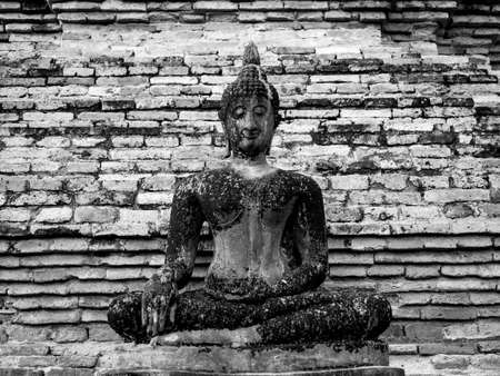 Ancient meditating buddha statue on old brick wall background at Wat Mahathat Temple in the precinct of Sukhothai Historical Park, black and white style.の写真素材