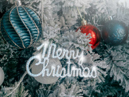 Christmas background. Merry Christmas, celebration words with balls decoration on fir tree covered by white snow, close up.の写真素材