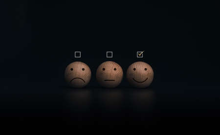 Check mark a checkbox on smiley emoticon face on the wooden balls on dark background. Customer service evaluation, rating, feedback, and satisfaction survey concept.の写真素材