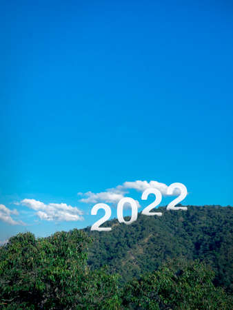 Happy New year 2022 with large letters on lush green fertile mountains, blue sky background with...