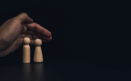 Insurance collateral concept. Hand protecting family wooden figures, male and female, couple on dark...