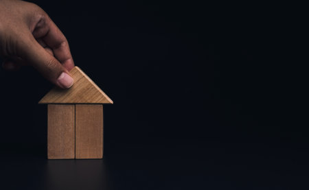 Hand building house with wooden blocks, laying of the roof on dark background with copy space. Property planning. House building construction symbol, eco style, loan concepts.の写真素材