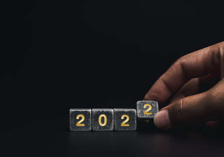 The year 2021 change to 2022 with the successful concept. Close-up hand flipping black cube blocks for change golden numbers from 2021 to 2022 on dark background with copy space, minimal style.の写真素材