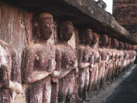 Row of ancient stucco, praying buddha statue at the base of old pagoda at Wat Mahathat Temple in the precinct of Sukhothai Historical Park, a UNESCO World Heritage Site in Thailand, close up.のeditorial素材