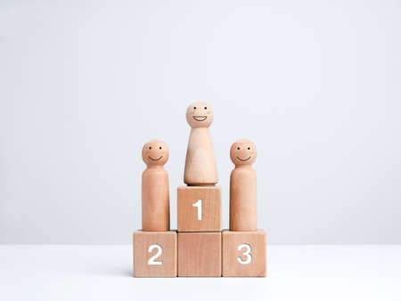 Business competition winner. Smiling female standing on the winner podium on the first award, wooden figure on wood cube block on white background. Women power, goals, success, and leadership concept.の写真素材