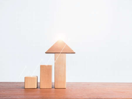 Three wooden blocks steps as a growth chart with arrow up on wood table on white grid graph background with copy space, minimal and eco style. Business growth success concept.の写真素材