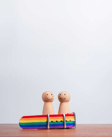 LGBT couple concept. Two wooden figures with happy smile faces standing together in the rainbow flag, wristband on wood table and background with copy space, vertical style. LGBT pride symbol.の写真素材
