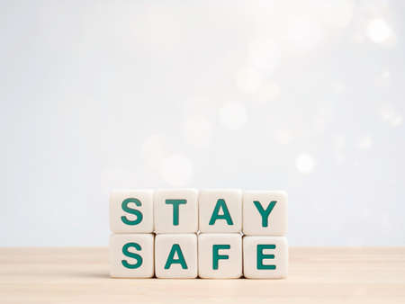 Stay safe concept. Green words, stay safe on white dice blocks on wooden desk on white background with bokeh and copy space. Staying at home to reduce risk of infection and spreading the virus.の写真素材