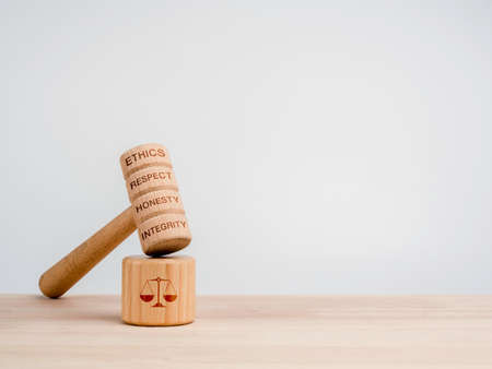 A wooden judge gavel with words, ethics, respect, honesty, and integrity with the soundboard with scales icon, toys on wooden table, white background with copy space, minimal style. Justice concept.の写真素材