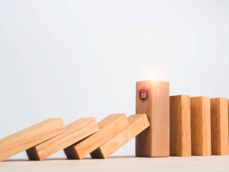 The big wooden block strong with shield security icon symbol standing protects falling domino pieces isolated on white. Stopping the domino effect. Business data management. Risk protection.の写真素材