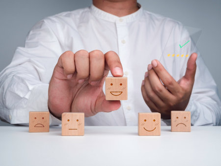 Customer service evaluation, feedback, client experience, and satisfaction survey concepts. The man picks the happy face wooden block and holds futuristic glass phone with five stars rating on screen.の写真素材