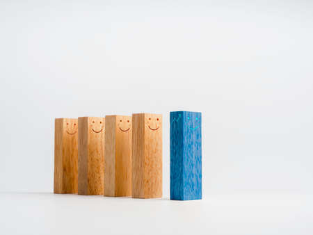 A unique blue wooden block with a happy face stands in front of the row of normal identical wood blocks isolated on a white background. Standing out from the crowd. Leadership and influencer concepts.の写真素材
