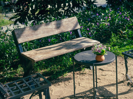 Terracotta pot with flowers decraotion on black round side table with emopty old wooden bench in the...
