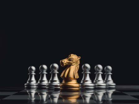 The golden horse, knight chess piece standing in front of silver pawn chess pieces on chessboard on...