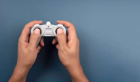 Hand holding and using silver retro style radio remote control for a toy isolated on blue background with copy space, top view. Game controller  joystick, flat lay, minimal style.の写真素材