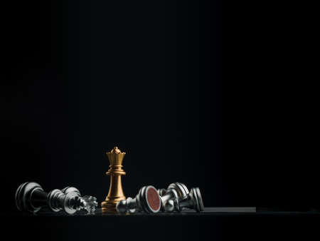The gold queen chess piece standing with falling silver pawn chess pieces on chessboard on dark...