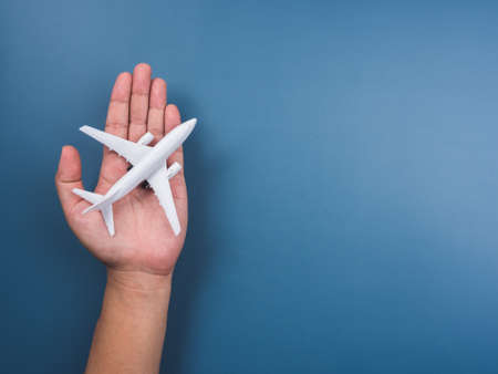 White plane toy model on hand on a blue background with copy space, top view, minimal style. White airplane, flat lay design. Flight, travel concept.の写真素材