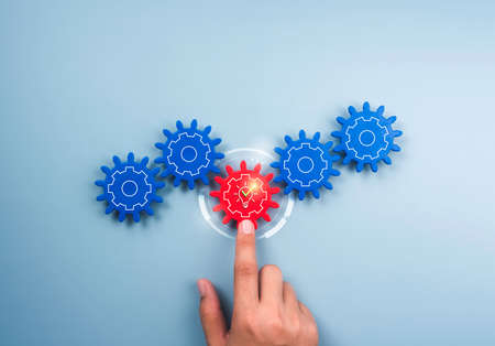 Business growth, solution, management, cooperation, innovation, leadership. Checkmark with Idea light bulb icon on cogwheels gears on blue background. Different red gear supports blue gears by hand.の写真素材