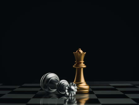 A golden queen chess piece standing with the win near a fallen silver queen chess piece on a chessboard on dark background. Leadership, winner, brave, competition, and business strategy concept.の写真素材