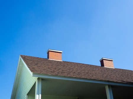 Close up two chimneys bricks on the roof of the light green wooden house against blue sky background on a sunny day with copy space.の写真素材