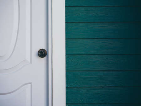 Close up the white vintage clean front door with iron knob near wood plank wall, dark green color with copy space.の写真素材