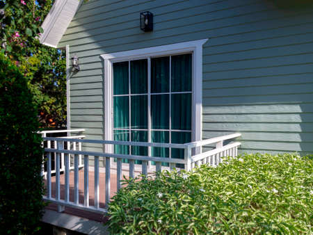 White house window with glass, green curtain on the empty terrace the small light green wooden...