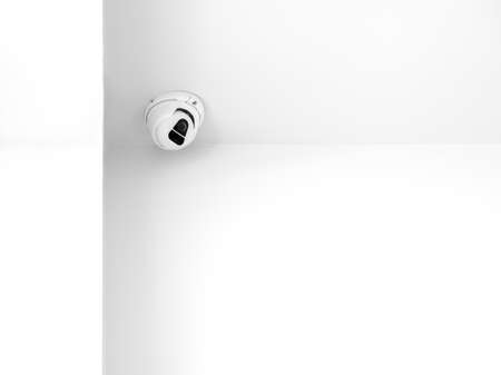 A white Indoor CCTV surveillance camera monitoring security on ceiling in the room corner inside the...