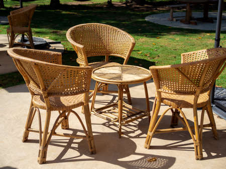 Empty rattan furniture, outdoor garden weave table set with round table and three chairs on the green concrete floor in the green yard, simple design.の写真素材