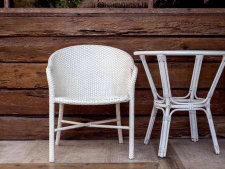 Empty modern white rattan furniture, outdoor garden weave chair and round side table on the natural log wood plank wall background at the terrace.の写真素材