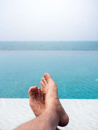 Close-up of the man's foot in the blue water on the tropical pool and sea view. Holiday, vacation summer background, vertical style.の写真素材