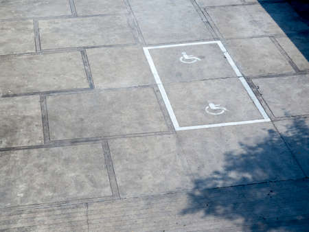The old white handicapped icon symbol on the ground shows a sign reserved for disabled persons in a...