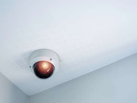 Digital security eye. A white round indoor CCTV surveillance camera monitoring security on ceiling...