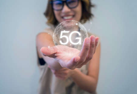 5G internet technology concept. Virtual 5G hologram with global connect icon appeared in happy Asian woman's hand who wearing eyeglasses on white background. Business network digital connection.の写真素材