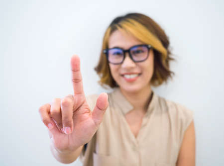 Closeup finger touch on virtual touch screen by happy smile Asian woman short hair wearing eye glasses with blue filter on white background. Hand point or press on empty space by businesswoman's hand.の写真素材