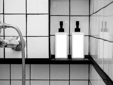 White blank labels mockup on two shower bottles, pump bottle with dispenser for liquid soap, shampoo, shower gel, side view. Close-up empty package label on containers on grid tiles wall in bathroom.の写真素材