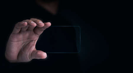 Future transparent glass phone Technology. Mock-up blank screen futuristic transparent smartphone in human hand on dark with copy space, horizontal. Future technology communication equipment.の写真素材