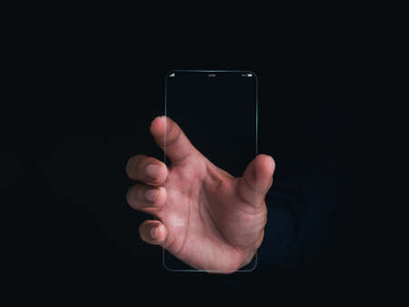 Futuristic transparent glass phone Technology. Super slim transparent future smartphone with vertical mock-up blank screen in hand on dark background.の写真素材