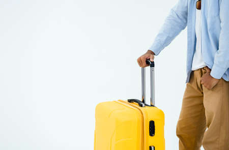 Ready to trip. Suitcase handle in young casual man's hand, blue jeans shirt and brown trousers isolated on white background with copy space. Summer vacation, holiday, tourist, journey concept.の写真素材