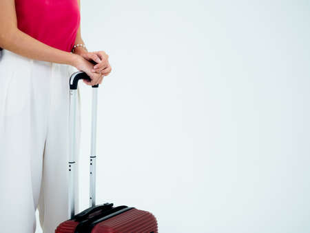 Ready to trip. Suitcase handle in young casual women's hand, pink sleeveless shirt and white trousers isolated on white background with copy space. Summer vacation, holiday, tourist, journey concept.の写真素材