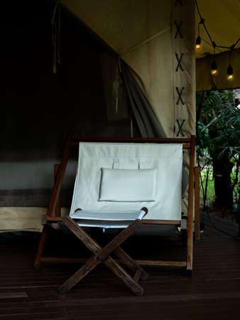Empty camping wooden chair with white fabric seat and footrest on the terrace in front of the room...