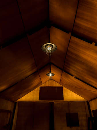 Old retro style lamp hanging on the ceiling inside the large glamping tent at a night. Lighting in the tent, vertical style.の写真素材