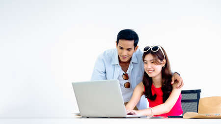 Happy Asian couple, young woman and man using laptop computer on desk together for flight booking, hotel room and trip information in office, ready to travel, happy holiday, summer vacation concept.の写真素材