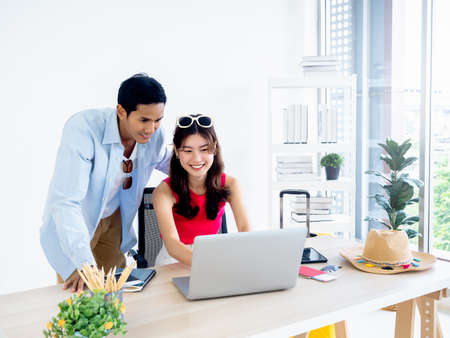 Happy Asian couple, young woman and man using laptop computer on desk together for flight booking,...