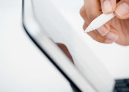 Close up white electronic pen or pencil in hand, write, draw or sign on digital tablet screen, computer isolated on white background. Business and technology concept. Working with tech device.の写真素材