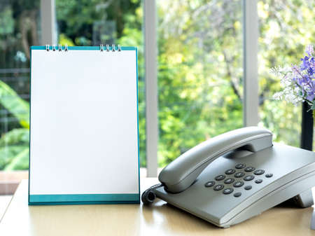 White blank desktop flip-top calendar template vertical style near the phone on wooden desk in...