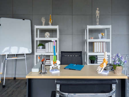Orthopedic doctor office background decorated with chairs, table with tools and medical equipment, skeleton, bone model on shelf and white board. Interior of modern doctor's office in clinic.の写真素材