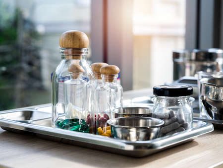 Close up set of vitamins and supplements in the small clear glass bottles in the steel medical tray on wooden table. Green, yellow, red, white vitamins group. Healthcare, and medical concepts.の写真素材