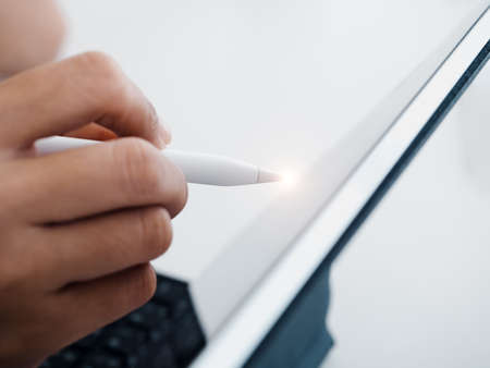 Close up white electronic pen or pencil in hand, write, draw or sign on digital tablet screen, computer isolated on white background. Business and technology concept. Working with tech device.の写真素材