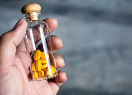 Close up yellow vitamins or supplements in the small clear glass bottle vials in person's hand with copy space. Hand holding vials with drug capsules. Healthcare, and medical concepts.の写真素材