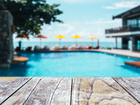 Close-up empty space on old wooden plank table or deck floor in front of the blurred pool, beach and open sky background on sunny day. Empty space for product at poolside, summer background.の写真素材